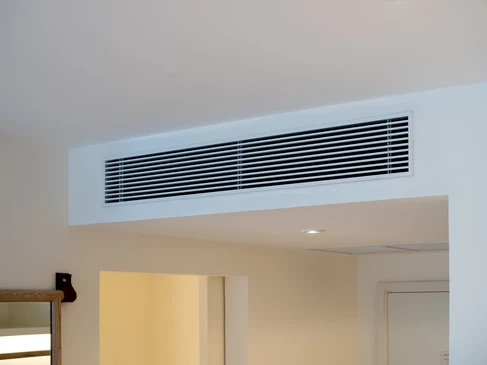Ouvrier en combinaison à carreaux travaille dans les combles d'une habitation, installant ou réparant un système de ventilation